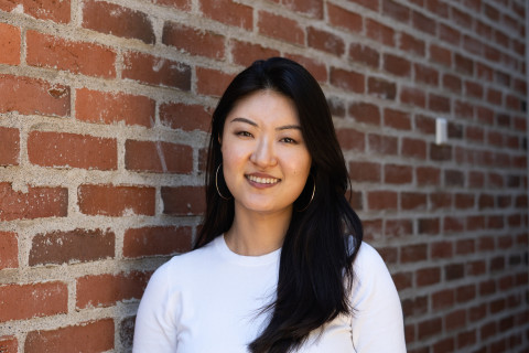 Female student smiling at the camera, red brick wall behind her.