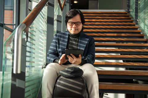 Young man sitting on the stairs, looking at the tablet device in his hands.