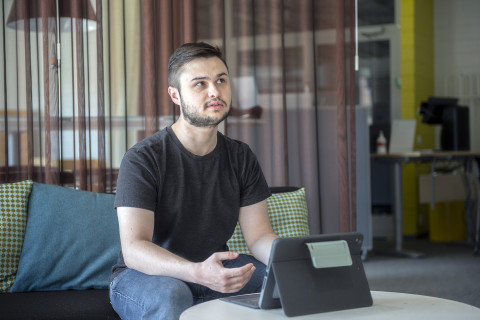 Young man sitting on a sofa, laptop in front of him on a small table.