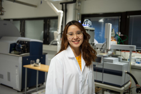 Young woman in a lab coat smiling, laboratory in the background.