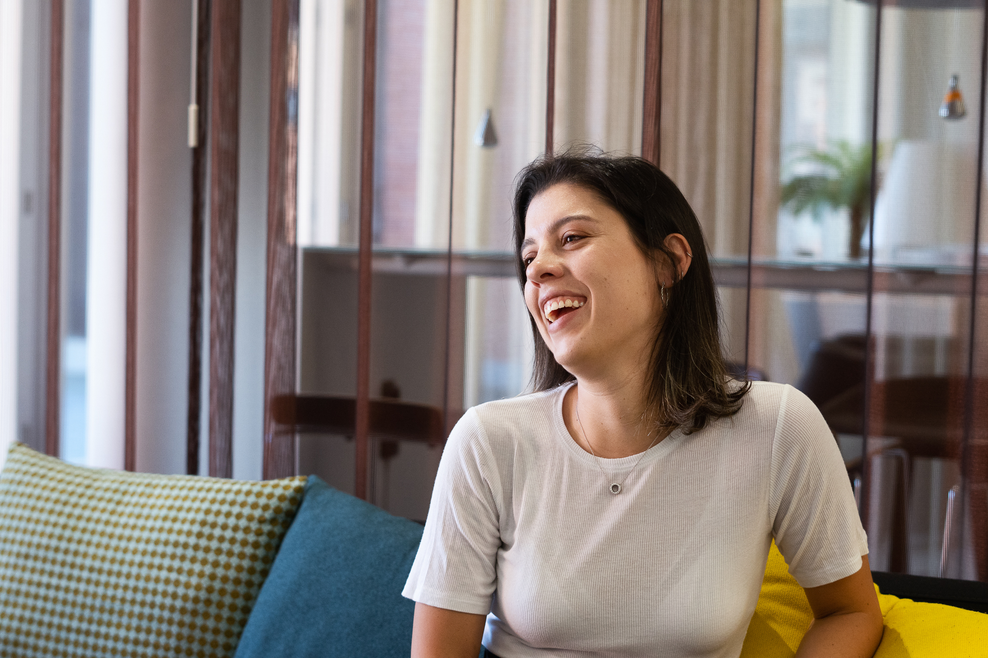 Nuori nainen istuu sohvalla, nauraa jollekin asialle kuvan ulkopuolella.