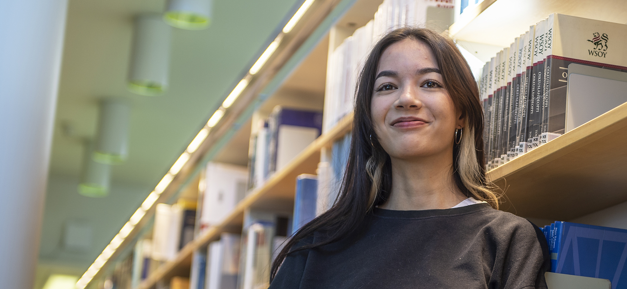 Nainen valaistun kirjahyllyn vierellä.