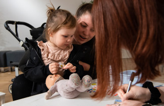 Nainen ja pieni lapsi käyttämässä pehmolelua nallesairaalassa.