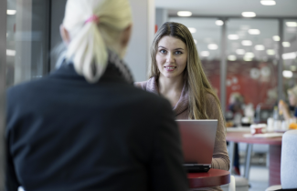 Nainen istuu kahvilassa tietokoneen kanssa
