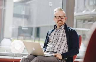 Mies istuu tuolissa kannettava sylissään