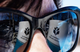 Kuvassa naisen aurinkolaseista heijastuu yliopiston logo