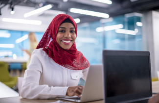 nainen hymyilee leveästi tietokoneen ääressä