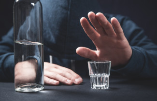 Pullo ja juomalasia poistyöntävä käsi pöydän ääressä.