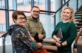 Three persons standing in front of a window.