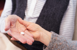 Lääkepilleri iäkkään henkilön kämmenellä.