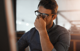 Mies hieroo väsyneitä silmiään toimistossa.