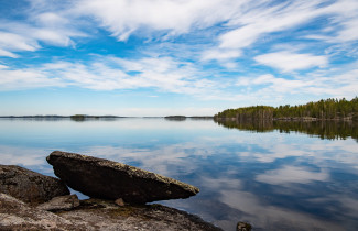 Järvi, kiviä, metsää ja pilvinen taivas.