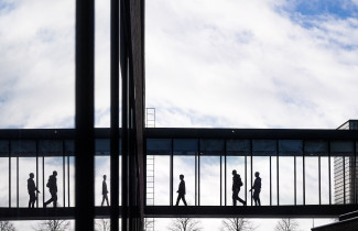 Ihmiset ylittämässä lasitettua käytävää rakennusten välillä.