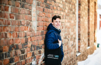 Mies nojaa seinään ja hymyilee kameralle talvella