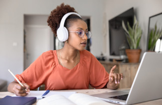 Opiskelija kuulokkeet päässä tietokoneen ääressä.