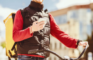 Ruokalähetti katsoo kännykkää pyörän selässä.