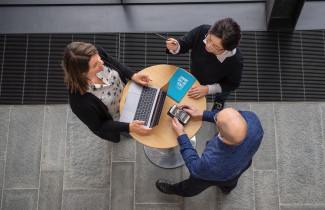 Kolme henkilöä neuvottelee pöydän ympärillä.