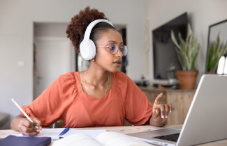 Opiskelija kuulokkeet päässä tietokoneen ääressä.