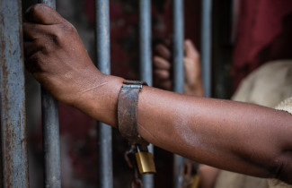Handcuffs on a person's hand and hands on bars.