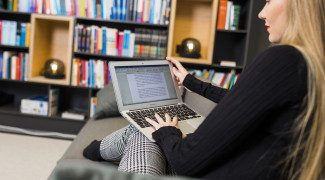 Nainen istuu sohvalla kannettava sylissään