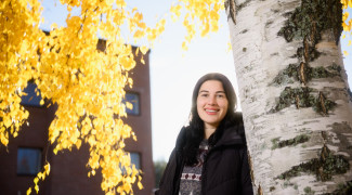 Student smiling on outside next to a birch