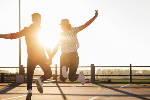 Photo of two people in the sun, holding hands and jumping from the ground.