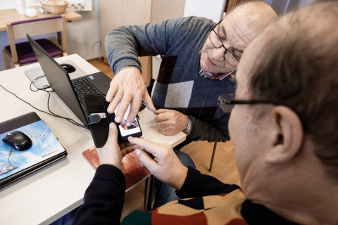 Photo of two older men using a laptop and a smart phone.