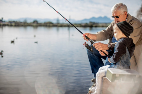 An old man and a young boy sitting on a pier and trying to catch fish.