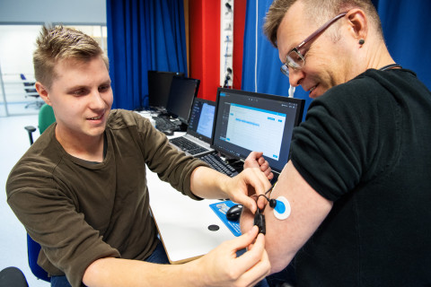 Tutkija asettaa anturia koehenkilön käsivarteen