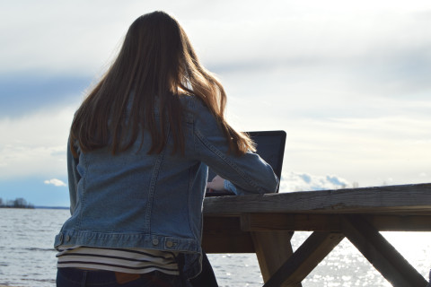 Nuori nainen kannettavan tietokoneen ääressä järven rannalla.