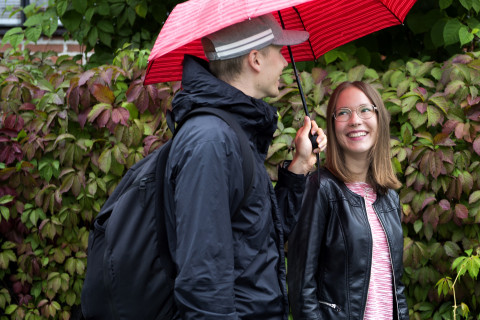 Opiskelijat kävelevät kampuksen ulkopuolella sateenvarjon kanssa