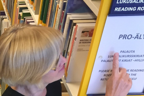 Kirjaston työtekijä osoittaa hyllynpäätykylttiä, jossa lukee aakkosvälitieto pro-äly.