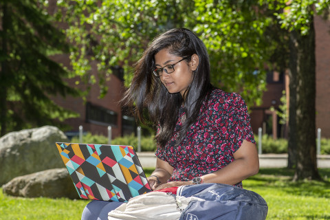 Nuori nainen istuu ulkona, työskentelee kannettavan tietokoneen kanssa.