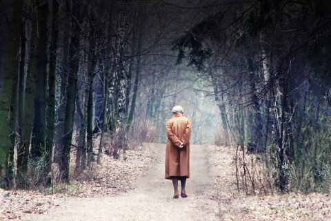 Vanha nainen kävelee metsätiellä.