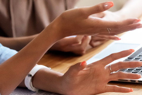 Hands of two women and a computer in a meeting.