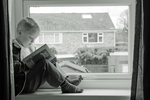 Poika istuu ikkunalaudalla ja lukee kirjaa.