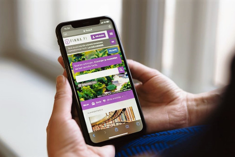 Ihminen pitelee molemmin käsin matkapuhelinta, jolla näkyy Finna.