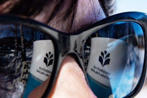 Kuvassa naisen aurinkolaseista heijastuu yliopiston logo