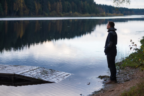 Yksinäinen mies seisoo järven rannalla.