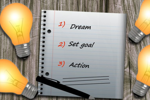 Muistilehtiö, hehkulamppuja. Lehtiössä teksti: 1) dream 2) set goal 3) action.