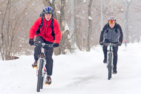 Kaksi henkilöä polkee polkupyörällä talvista tietä.
