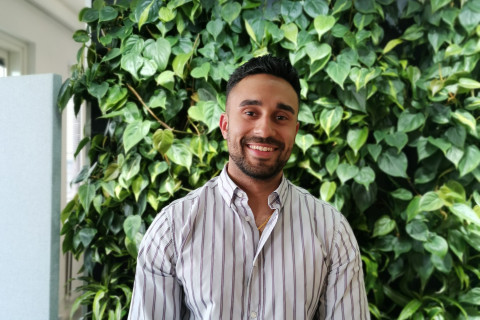 Opiskelija hymyilee kameralle takanaan vihertävä tausta.