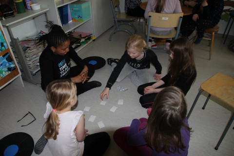 Teacher and pupils sitting on the floor playing cards.