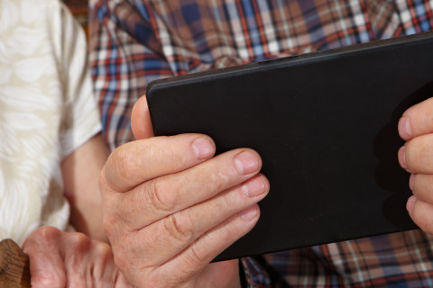 Iäkäs ihminen pitelee tablet-tietokonetta käsissään.