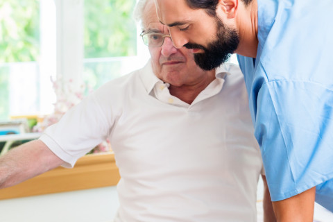 Hoitaja avustaa vanhaa miestä.