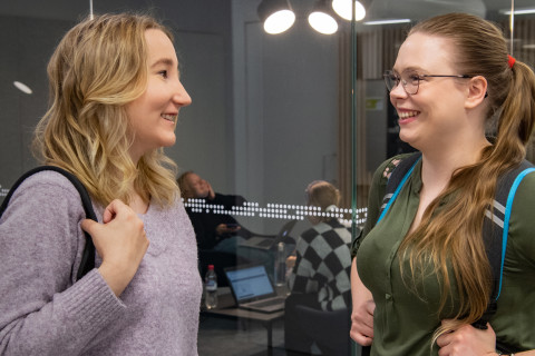 Kaksi opiskelijaa keskustelee iloisesti kampuksella.