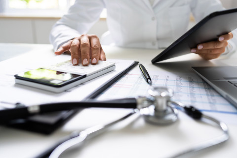 Lääkäri, tablet-tietokone, laskin ja stetoskooppi.