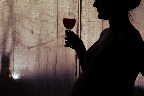 Raskaana oleva nainen viinilasi kädessään.