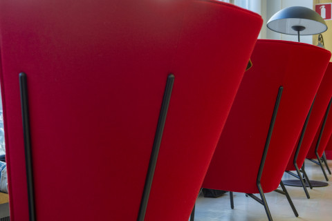 Punaisia nojatuoleja Joensuun kampuskirjastossa. Etualalla olevassa tuolissa istuu henkiläö, joka on riisunut kengät ja nostanut jalat ylös.