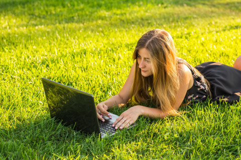 Nainen opiskelee nurmikolla tietokoneella. 